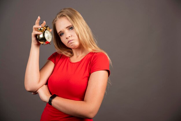 Mujer cansada de pie con reloj sobre fondo oscuro. Foto de alta calidad