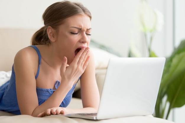 Mujer cansada que bosteza después de demasiado tiempo de trabajo en la computadora portátil