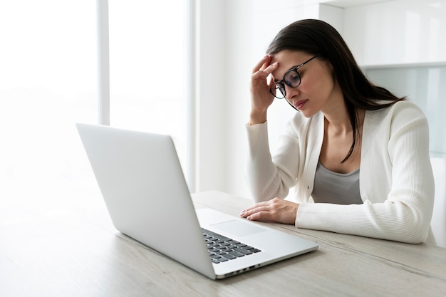 Mujer cansada de tiro medio que trabaja con una computadora portátil