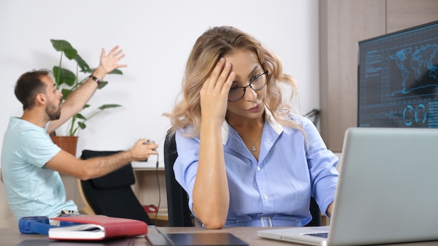 Mujer cansada trabajando en la computadora mientras su esposo está jugando videojuegos en el fondo