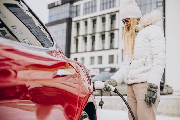 Mujer cargando coche eléctrico rojo, en época de invierno