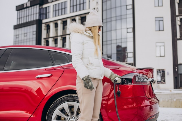 Mujer cargando coche eléctrico rojo, en época de invierno