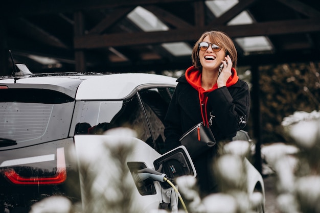 Mujer cargando electro car y hablando por teléfono