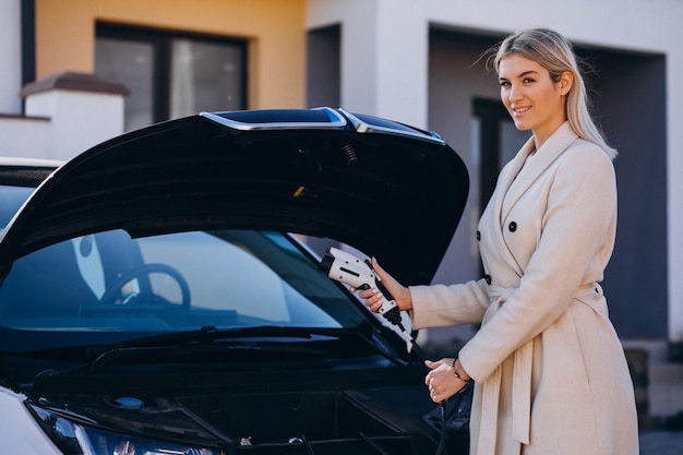 Mujer cargando electro car por su casa y sosteniendo el cargador