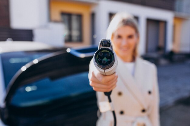 Mujer cargando electro car por su casa y sosteniendo el cargador