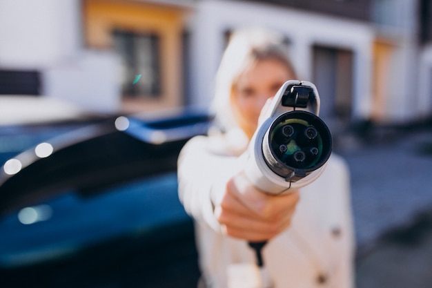 Mujer cargando electro car por su casa y sosteniendo el cargador