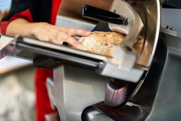 Mujer carnicero corte york jamón en una máquina de corte