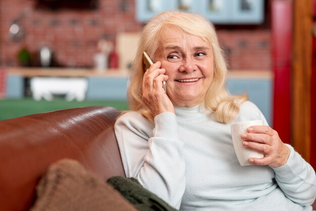 Mujer en casa bebiendo té y usando el teléfono