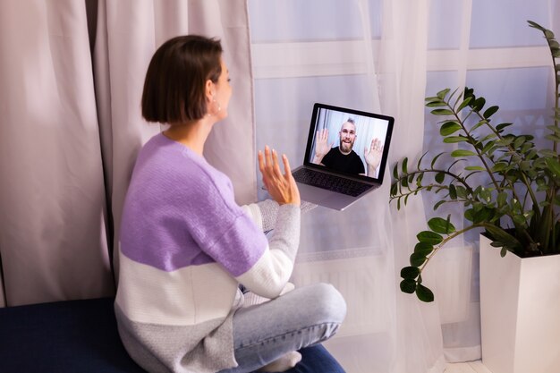 Mujer en casa cara a cara videollamada a su novio esposo de amigos, chateando en línea desde la computadora portátil