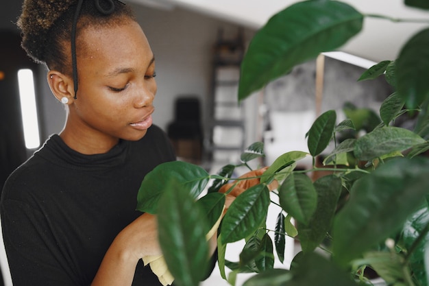 Mujer en casa. Chica con un suéter negro. La mujer africana usa el trapo. Persona con maceta.