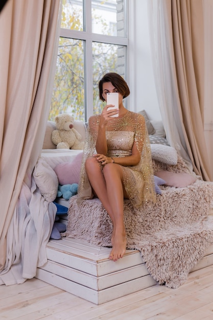 Mujer en casa en el dormitorio vistiendo traje de noche de Navidad, tomando foto selfie