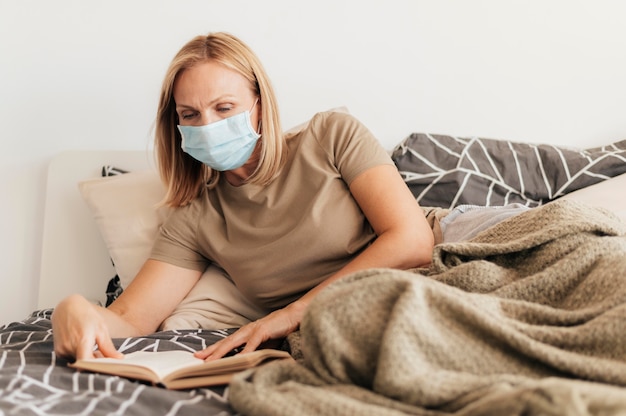 Mujer en casa con libro de lectura de máscara médica