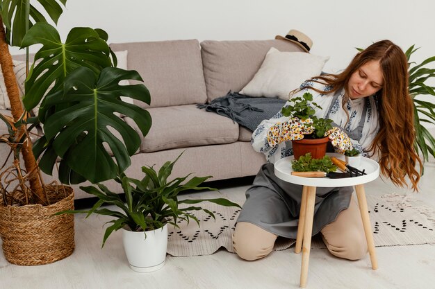 Mujer en casa con maceta de plantas y herramienta de jardinería