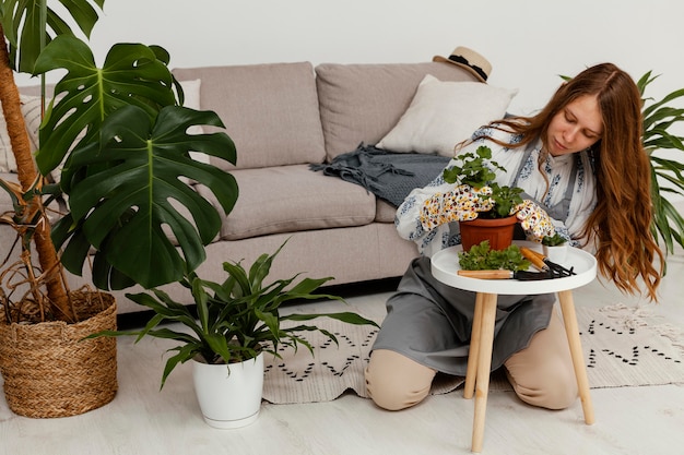 Mujer en casa con maceta de plantas y herramienta de jardinería