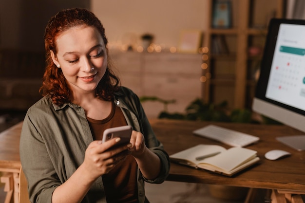 Foto gratuita mujer en casa con smartphone frente a la computadora