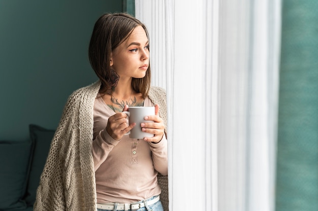 Mujer en casa tomando café y mirando por la ventana durante la pandemia