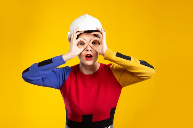 Mujer en casco de construcción muestra gafas con dedos