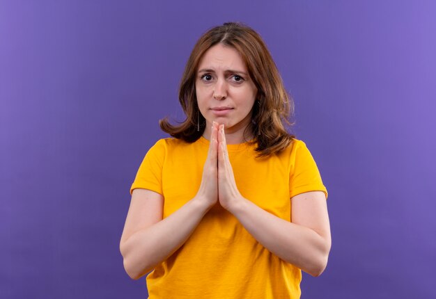 Mujer casual joven ansiosa poniendo las manos en gesto de oración en el espacio púrpura aislado con espacio de copia