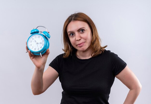 Mujer casual joven complacida que sostiene el reloj de alarma en el espacio en blanco aislado