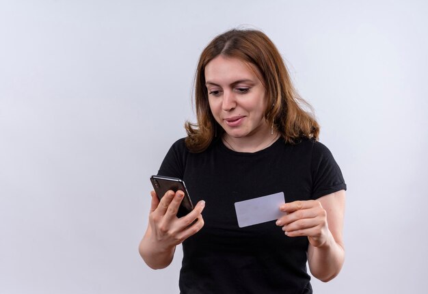 Mujer casual joven complacida con teléfono móvil y tarjeta de crédito en un espacio en blanco aislado con espacio de copia