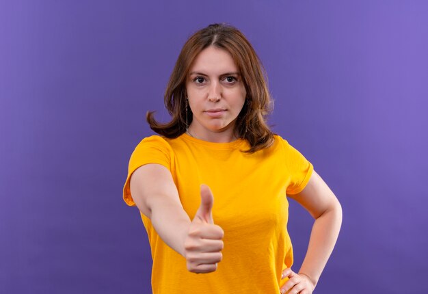 Mujer casual joven confiada que muestra el pulgar hacia arriba en el espacio púrpura aislado con espacio de copia