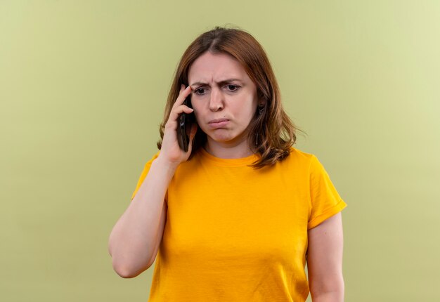 Mujer casual joven disgustada hablando por teléfono en la pared verde aislada con espacio de copia