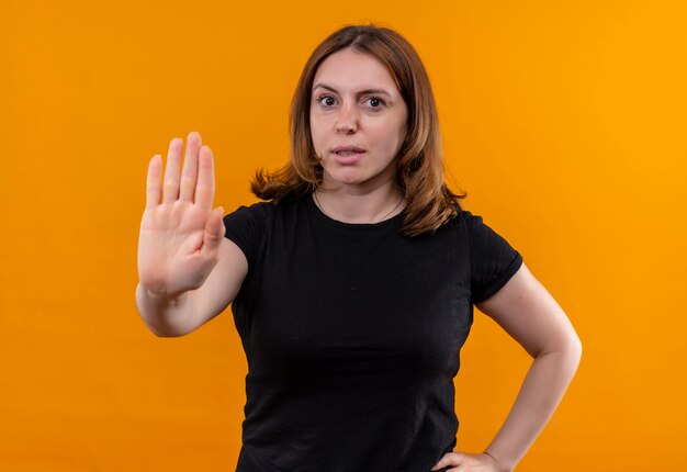 Mujer casual joven disgustada que gesticula parada con la mano en la cintura en la pared naranja aislada