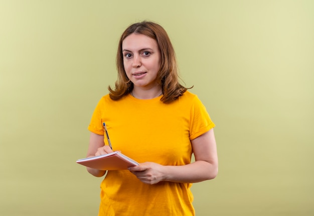 Mujer casual joven escribiendo algo en el bloc de notas en la pared verde aislada con espacio de copia