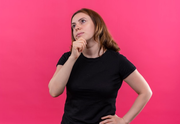 Mujer casual joven pensativa con la mano en la barbilla y en la cintura en la pared rosa aislada