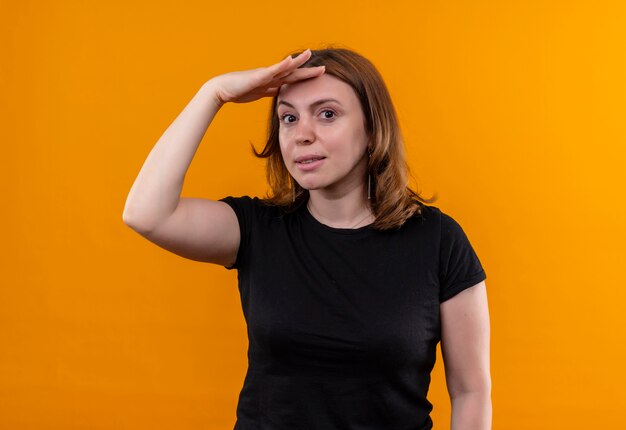 Mujer casual joven poniendo la mano en la frente y mirando en la pared naranja aislada