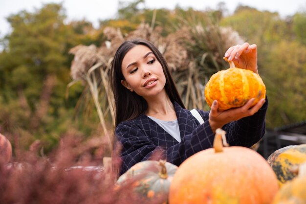 Mujer casual joven que elige cuidadosamente la calabaza para el día de Halloween en la tienda de la granja de otoño al aire libre