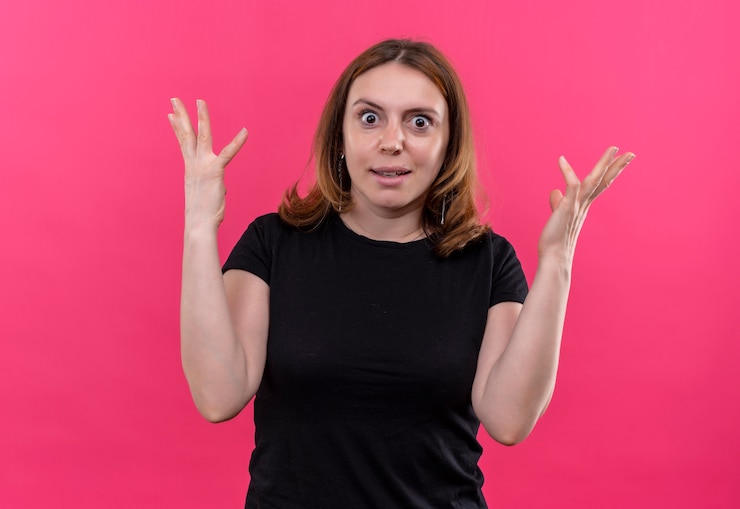 Foto gratuito mujer casual joven sorprendida con las manos levantadas en la pared rosada aislada