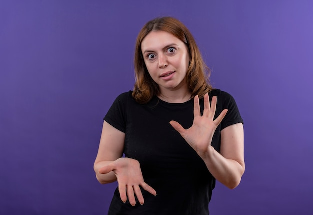 Mujer casual joven sorprendida que muestra las manos vacías en la pared púrpura aislada con el espacio de la copia