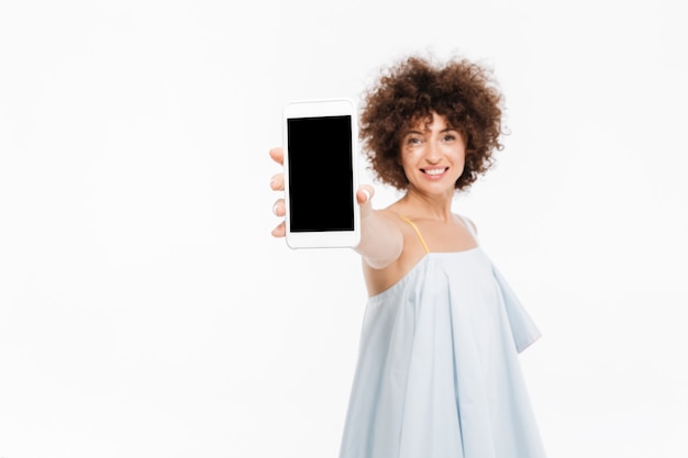 Mujer casual sonriente que muestra el teléfono móvil de la pantalla en blanco