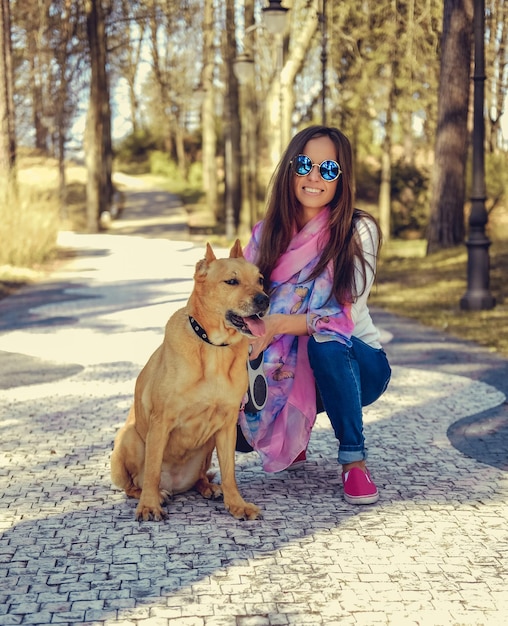 Mujer casual sonriente con su perro pitbull marrón en un parque.