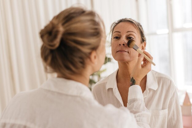 Mujer caucásica bastante adulta con camisa blanca utiliza los servicios de maquilladora, preparándose para la reunión. Belleza natural, concepto de cuidado de la piel.