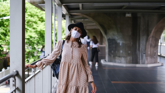 Mujer caucásica caminando en el cruce del metro en mascarilla médica mientras la pandemia en la ciudad de Bangkok.