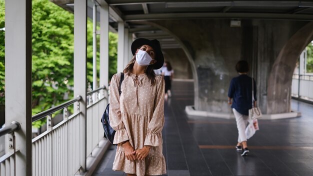 Mujer caucásica caminando en el cruce del metro en mascarilla médica mientras la pandemia en la ciudad de Bangkok.