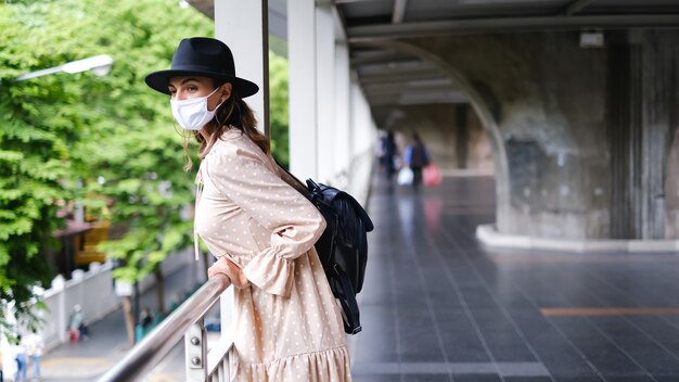 Mujer caucásica caminando en el cruce del metro en mascarilla médica mientras la pandemia en la ciudad de Bangkok.