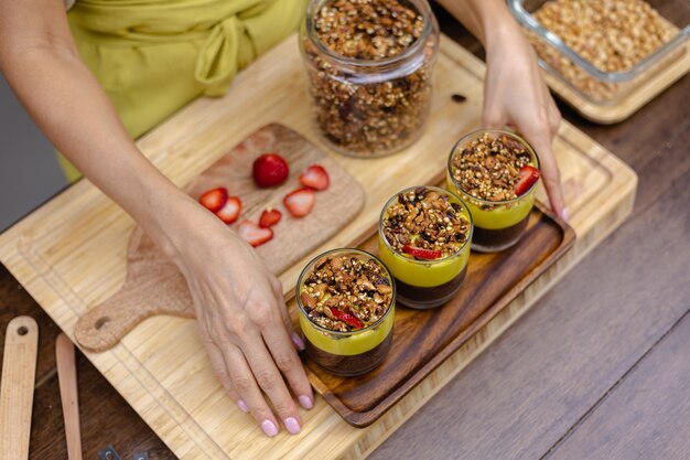 Mujer caucásica en la cocina hace budines de chía con mermelada de mango. Postre elaborado con leche de almendras, semillas de chía, cacao, mermelada de mango y granola.