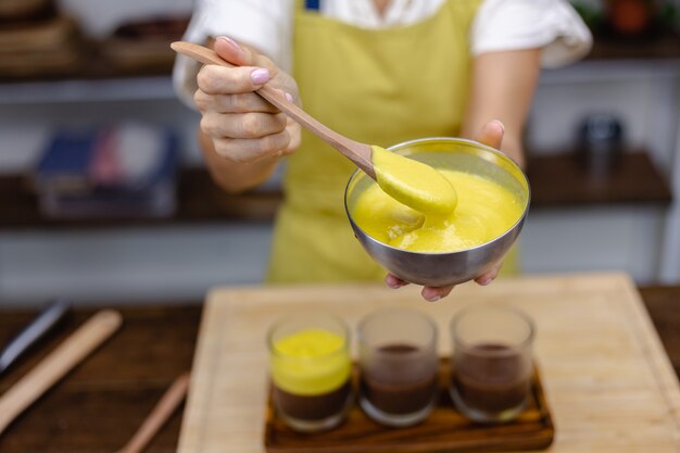 Mujer caucásica en la cocina hace budines de chía con mermelada de mango. Postre elaborado con leche de almendras, semillas de chía, cacao, mermelada de mango y granola.