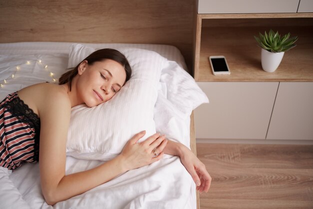 Mujer caucásica durmiendo en la cama. Lady disfruta de ropa de cama suave y fresca y colchón en el dormitorio