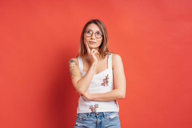 Mujer caucásica con gafas pensando e imaginación aislado en la pared roja