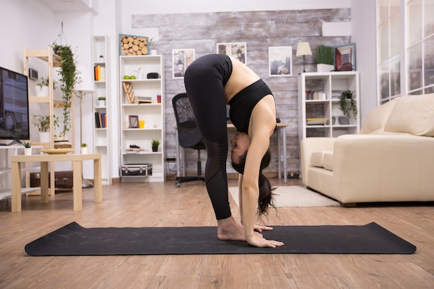 Mujer caucásica haciendo pose de flexibilidad de yoga en la estera en la sala de estar. Estilo de vida pacífico.