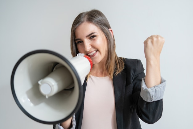 Mujer caucásica joven positiva con el megáfono que muestra éxito