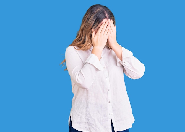 Mujer caucásica joven con ropa informal con expresión triste cubriendo la cara con las manos mientras llora. concepto de depresión.