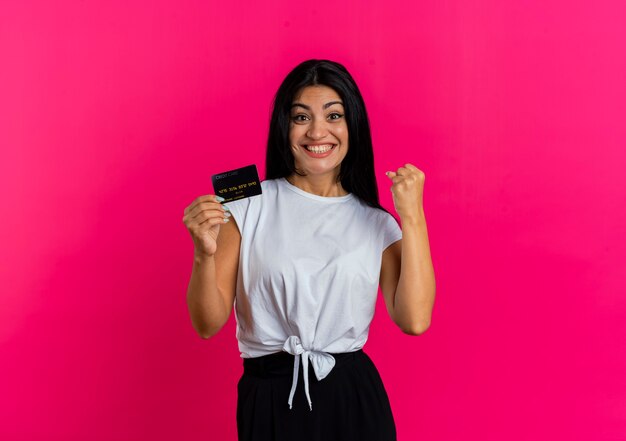 Mujer caucásica joven sonriente emocionada sostiene el teléfono y mantiene el puño