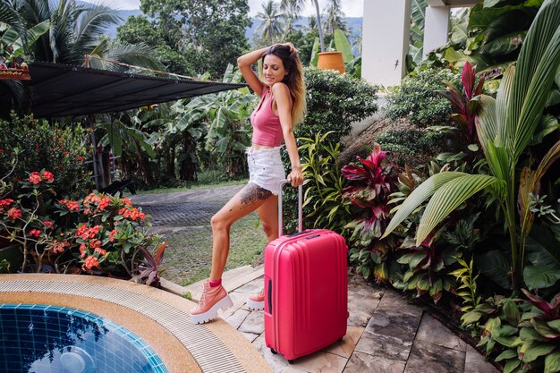 Mujer caucásica con maleta rosa grande de vacaciones en un país tropical