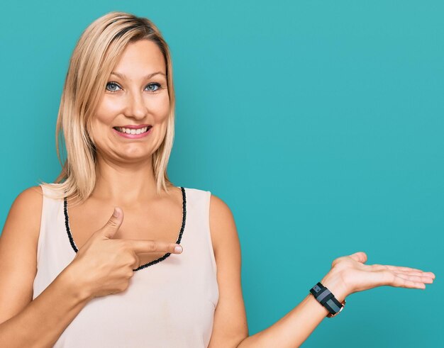 Mujer caucásica de mediana edad con ropa informal asombrada y sonriendo a la cámara mientras presenta con la mano y señala con el dedo.
