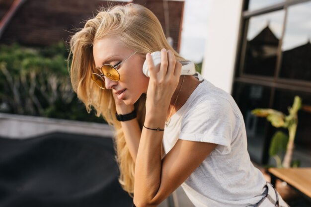 Mujer caucásica pensativa en auriculares blancos escuchando música al aire libre.